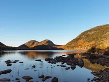 The Bubbles and autumn woodland reflected in Jordan Pond, with rocks along the south shore.