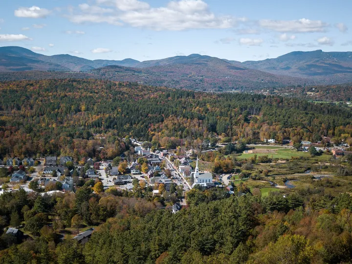Aerial view of Stowe’s white church steeple, village streets and autumn hills in Vermont.